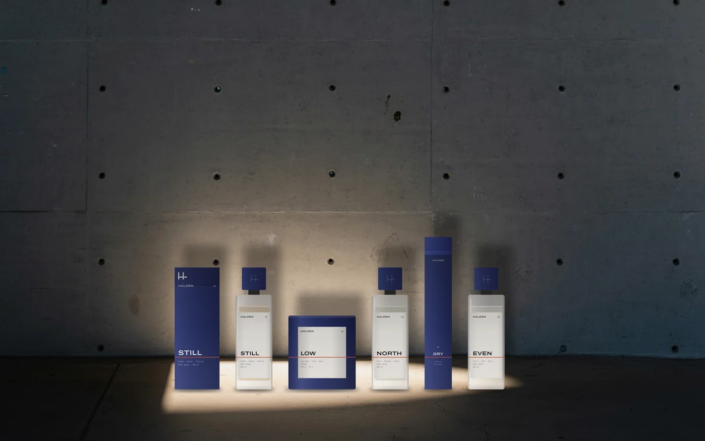 The Halden family, an outer box, three frosted room sprays, a blue candle and an incense box, standing in a pool of light against a board-marked concrete wall; a thin orange line crosses every object at the same height