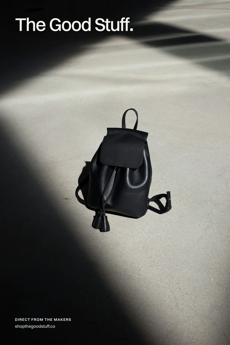 Campaign poster: a black leather backpack in a shaft of sunlight, with The Good Stuff wordmark set in the shadow above it