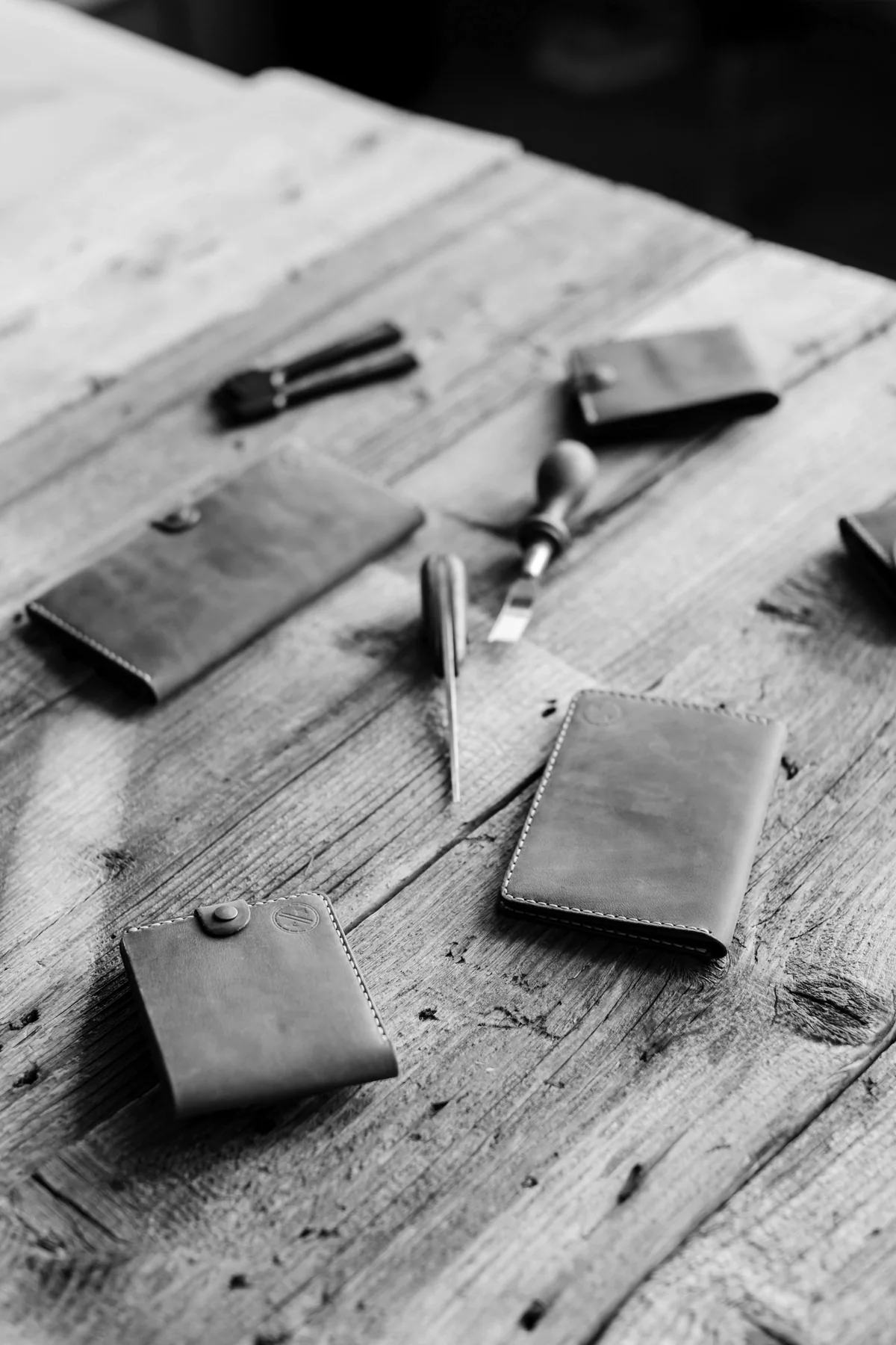 A few leather wallets and tools laid out on a workbench, in black and white