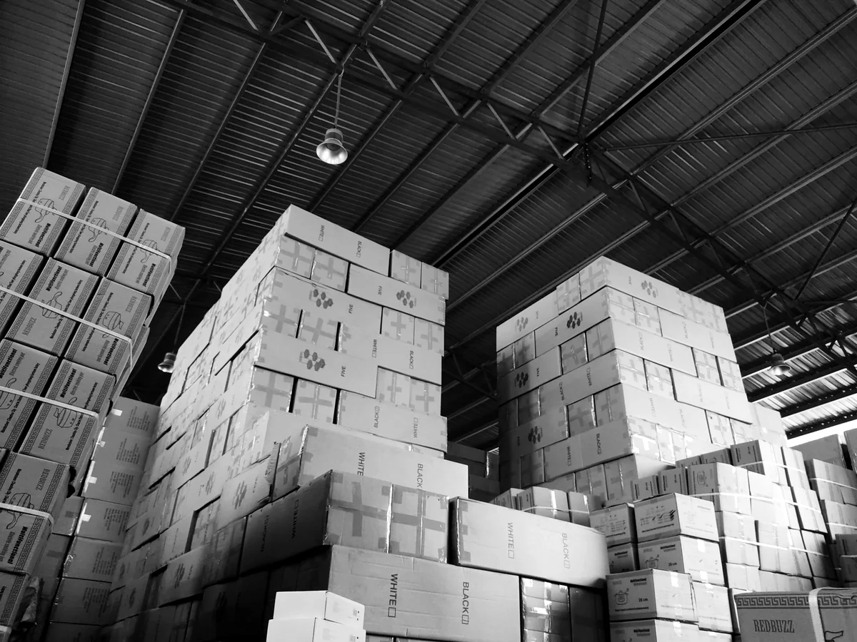 Cartons stacked to the roof of a warehouse, in black and white
