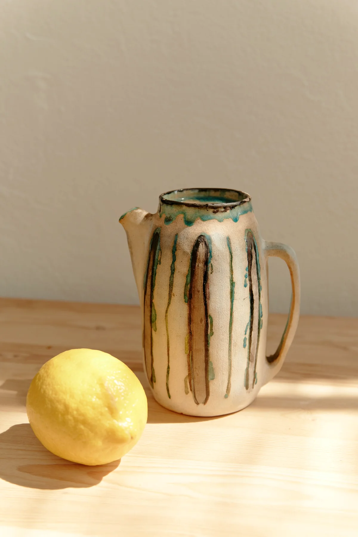 A striped stoneware jug and a lemon on a wooden table in warm light