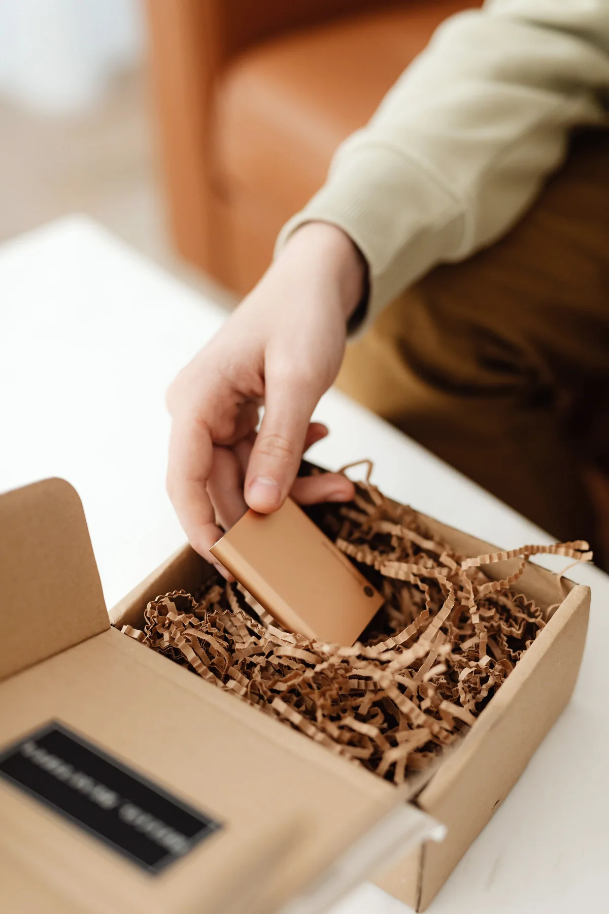 A hand placing an item into a kraft box filled with paper