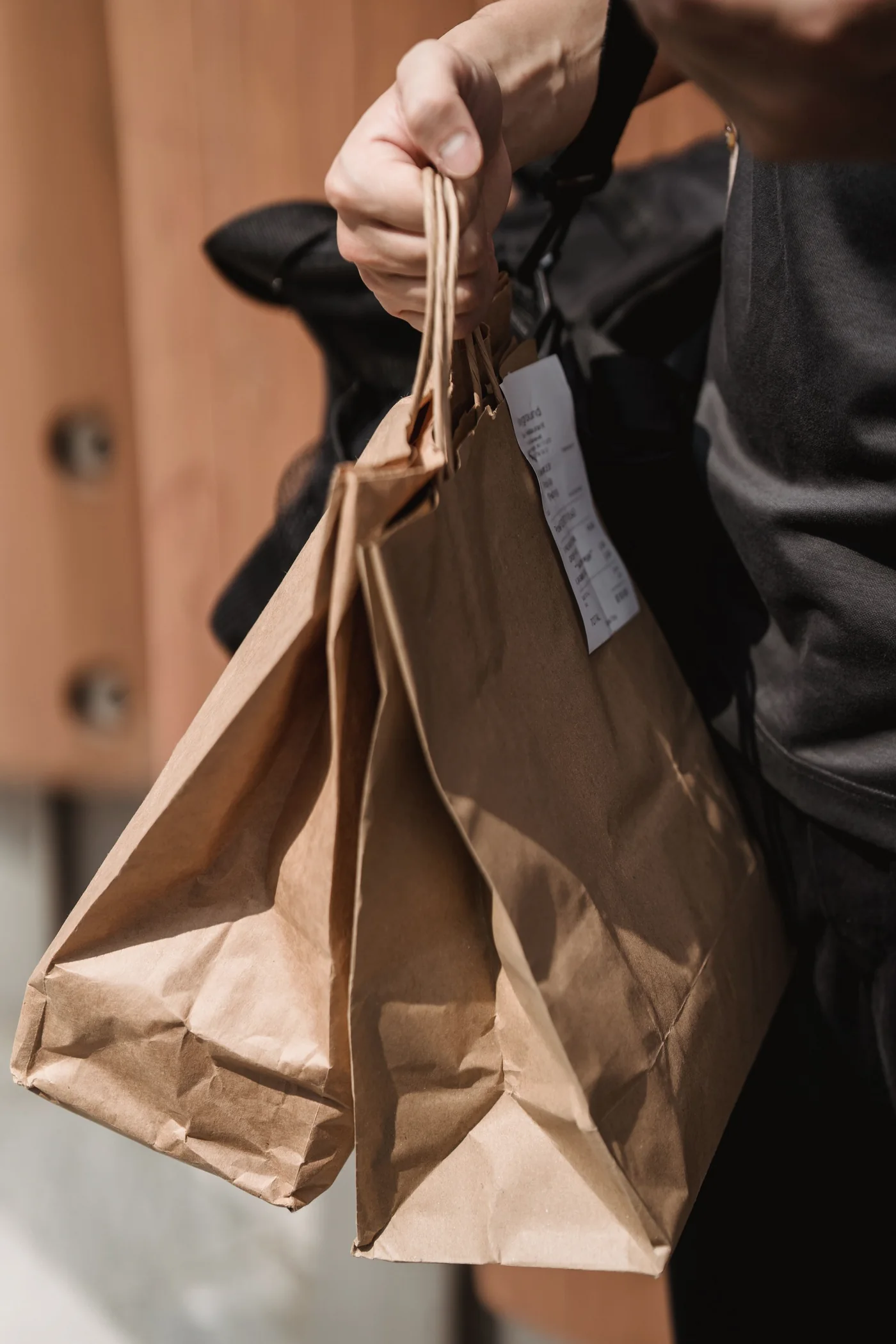 A hand carrying two plain kraft paper shopping bags
