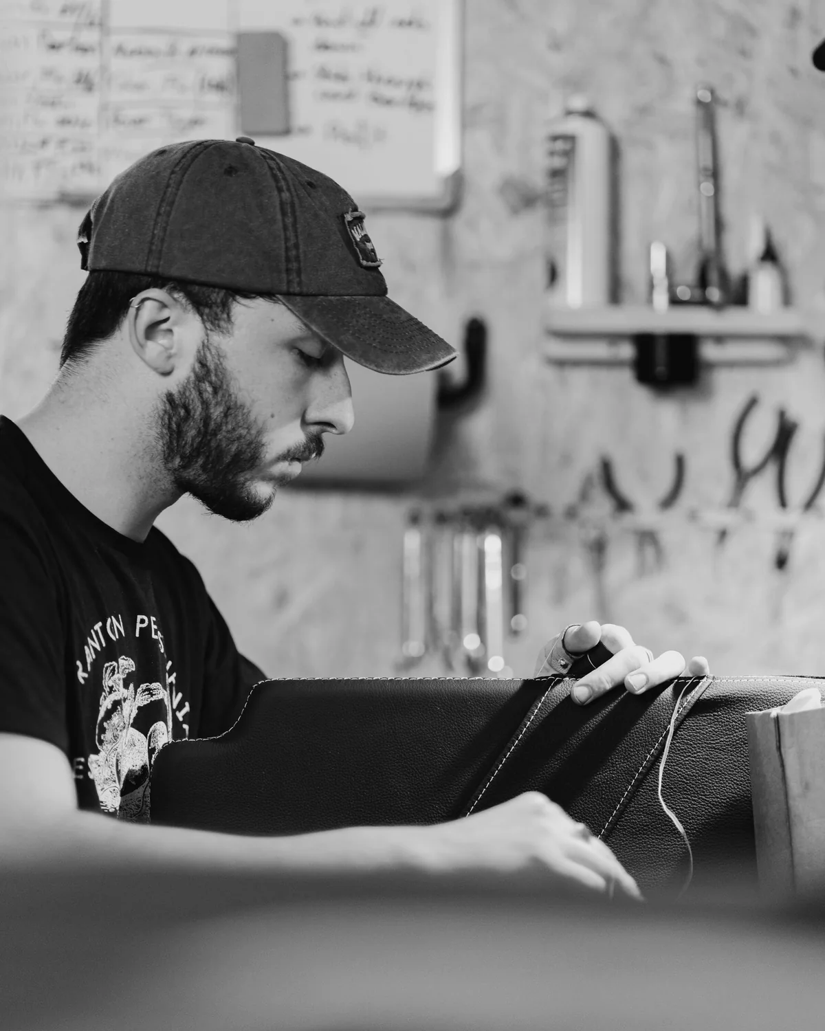 A maker stitching leather in a small workshop, in black and white