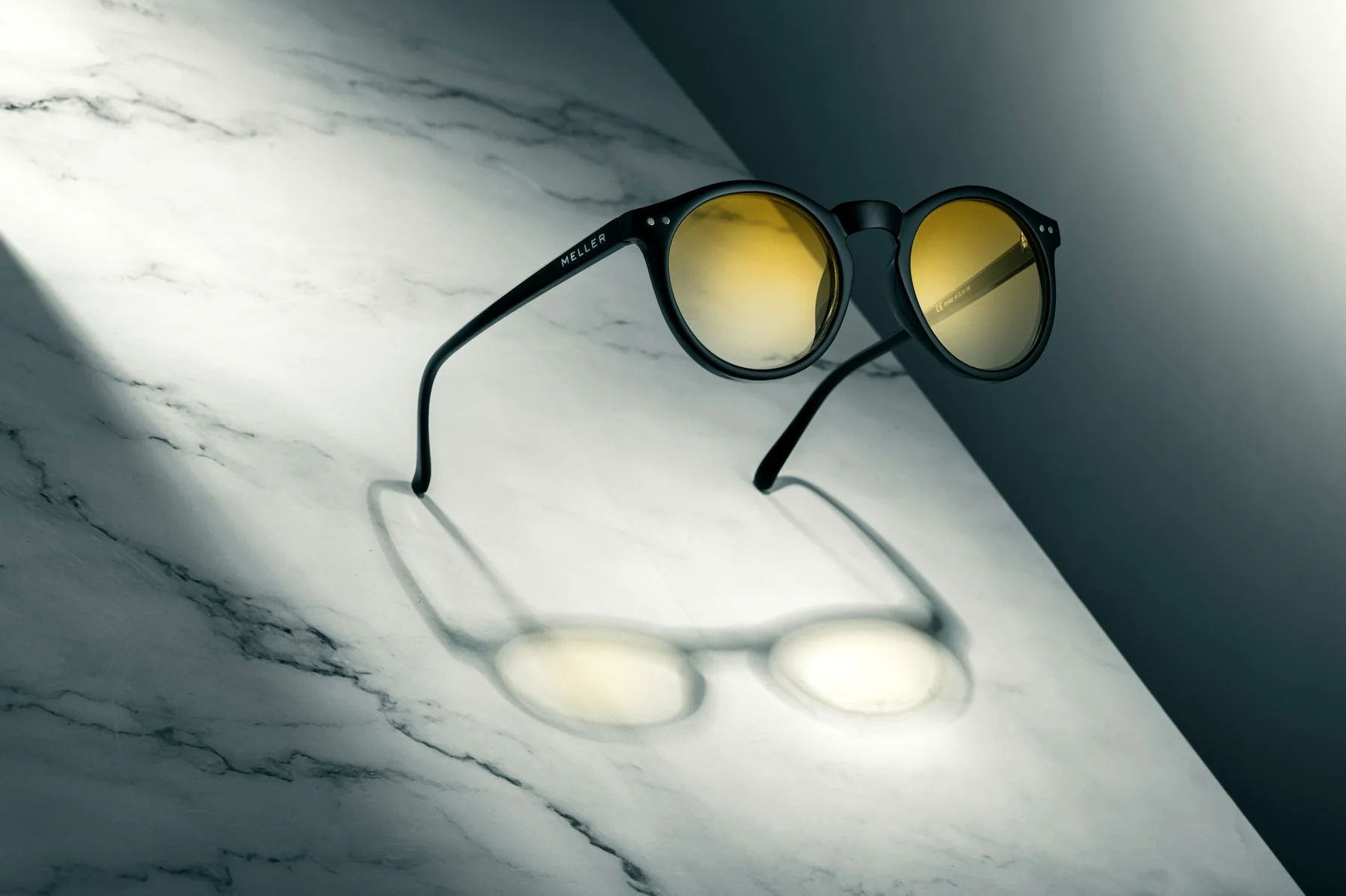 Black sunglasses with amber lenses on white marble, their shadow cast across the stone