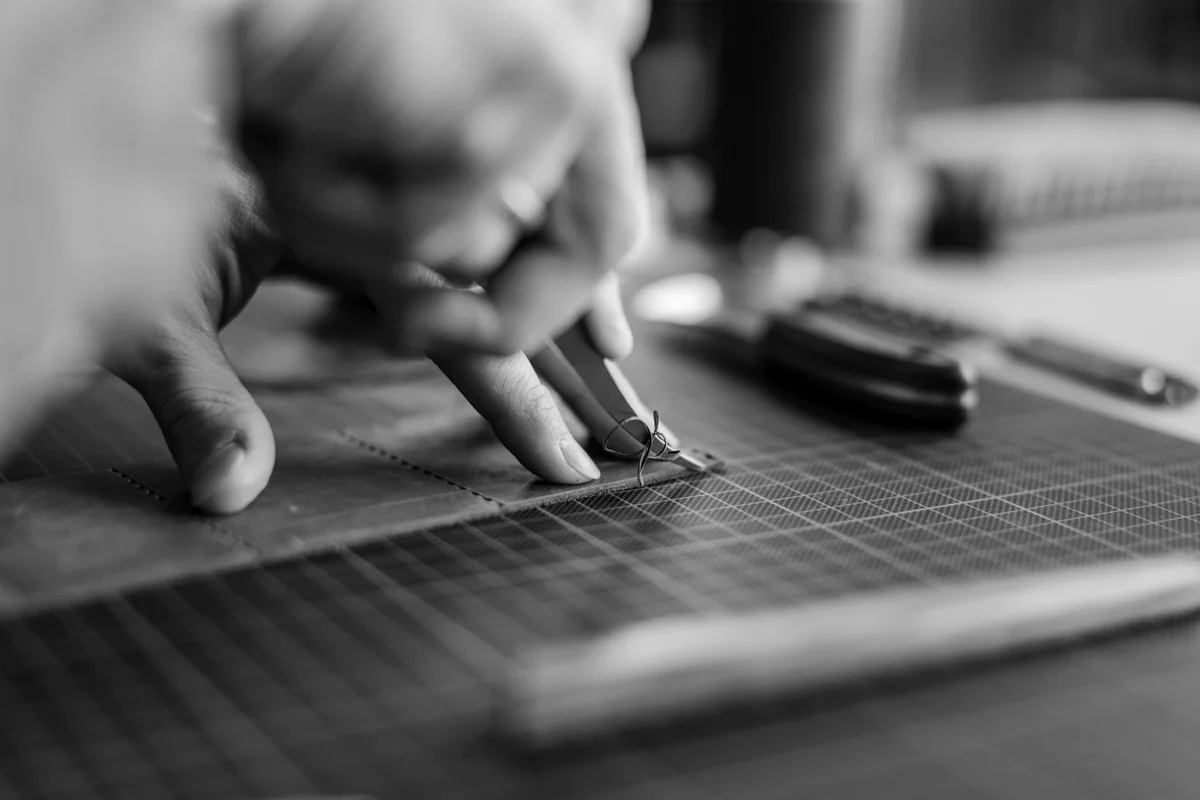 Hands cutting a strip of leather on a cutting mat, in black and white